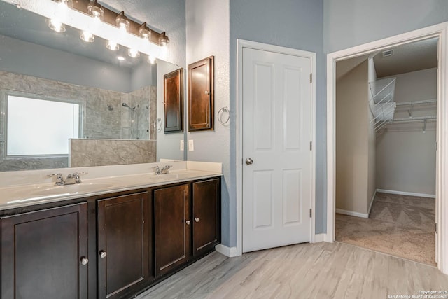 bathroom with a sink, double vanity, wood finished floors, and tiled shower