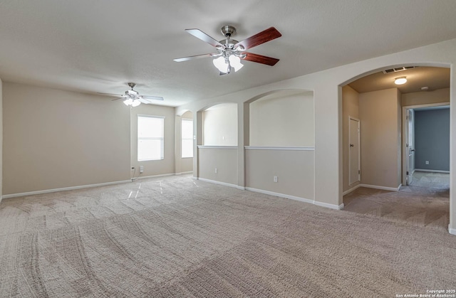 empty room featuring arched walkways, baseboards, ceiling fan, and carpet floors