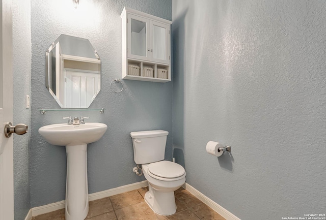 bathroom featuring toilet, a sink, tile patterned flooring, baseboards, and a textured wall