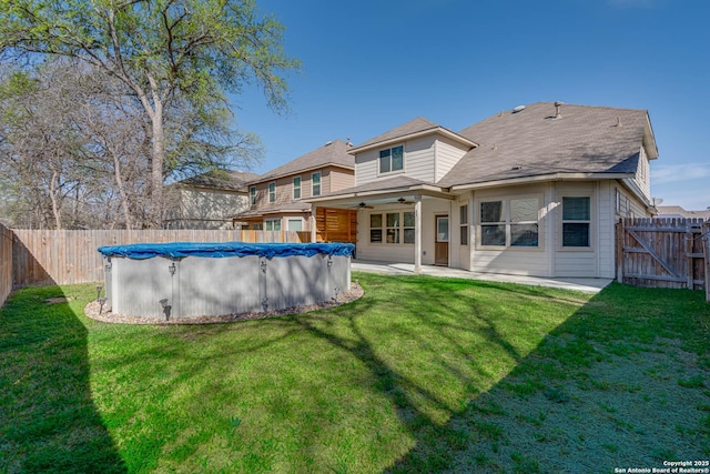 back of house featuring a ceiling fan, a fenced in pool, a fenced backyard, and a lawn