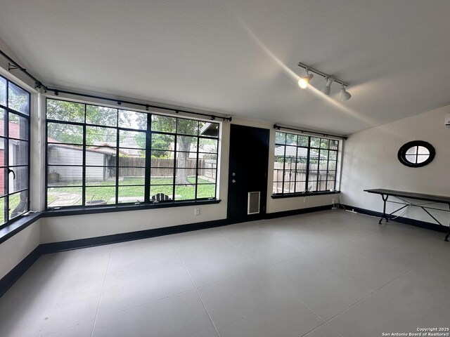 unfurnished room with track lighting, baseboards, and plenty of natural light
