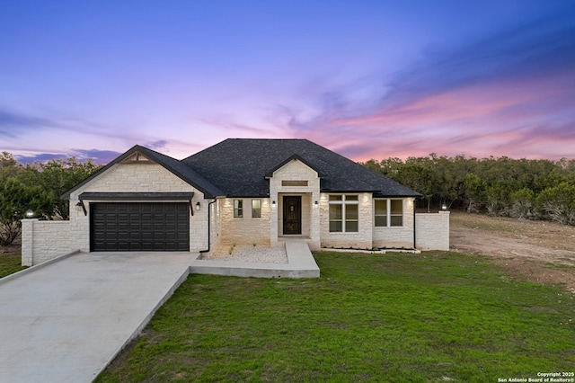 view of front of home featuring roof with shingles, concrete driveway, a garage, stone siding, and a lawn