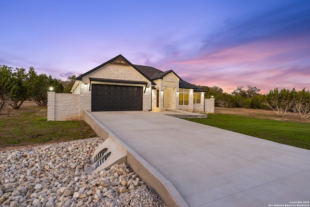 view of front of house featuring a garage, stone siding, a lawn, and driveway