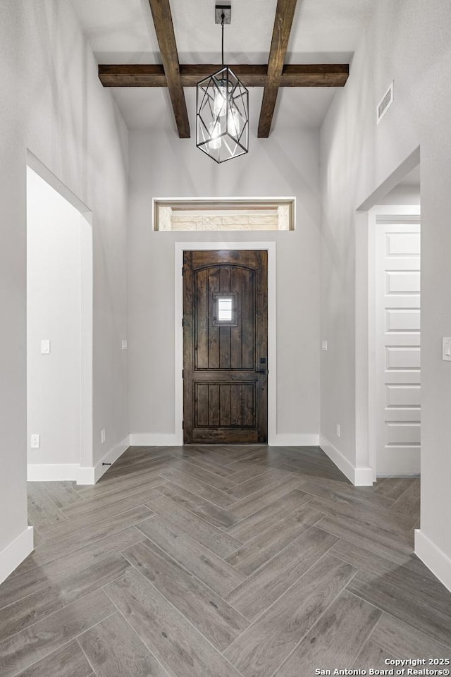 foyer entrance with beam ceiling, visible vents, and baseboards