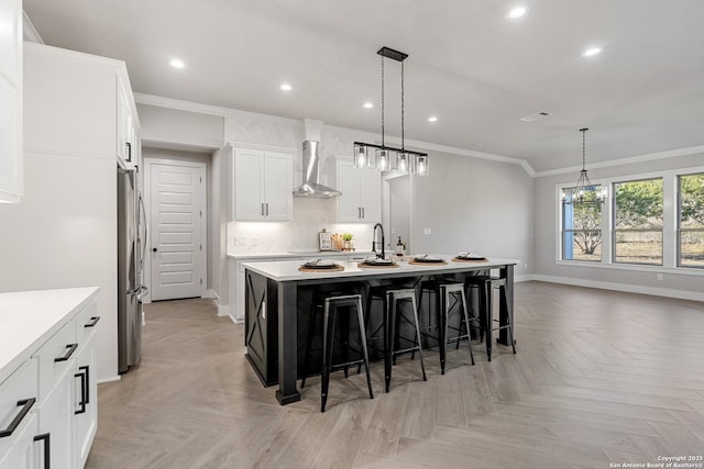 kitchen with an island with sink, ornamental molding, a kitchen bar, wall chimney exhaust hood, and tasteful backsplash