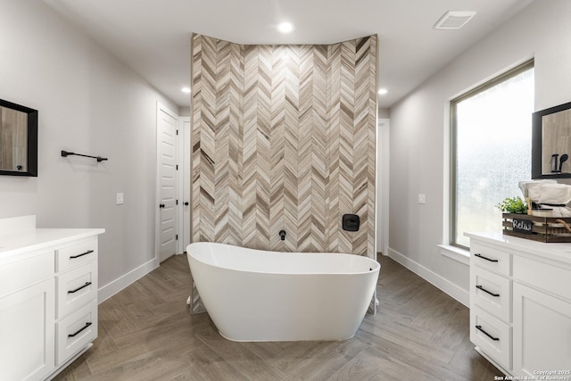 full bath featuring an accent wall, baseboards, a freestanding bath, recessed lighting, and vanity