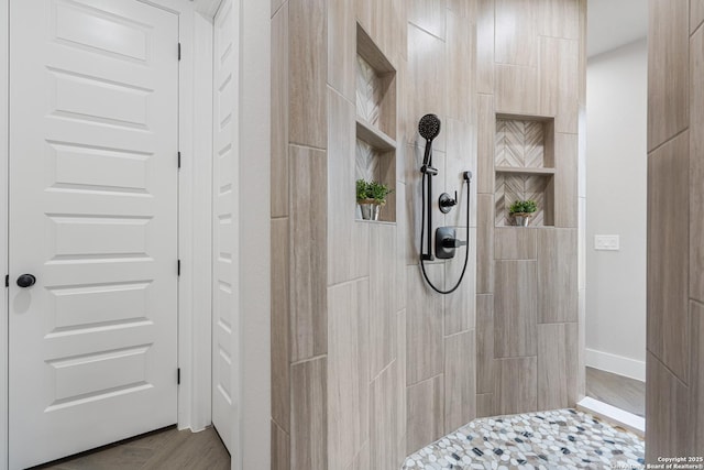 bathroom with baseboards, tiled shower, and wood finished floors