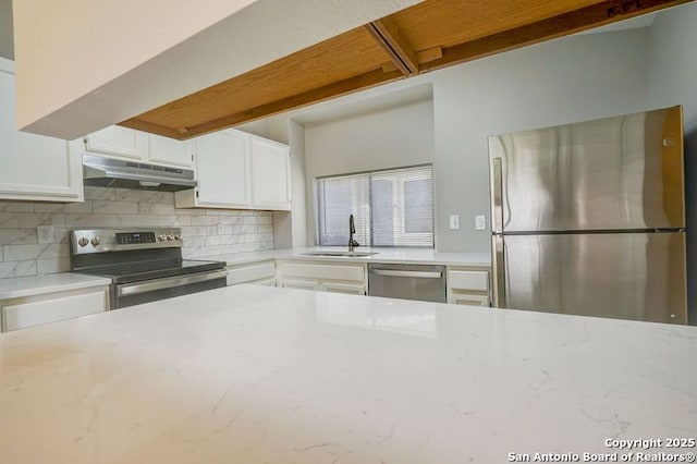 kitchen with light stone countertops, under cabinet range hood, appliances with stainless steel finishes, white cabinetry, and a sink