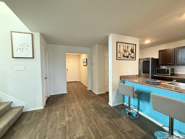 kitchen featuring stainless steel appliances, baseboards, dark brown cabinets, and dark wood-style floors