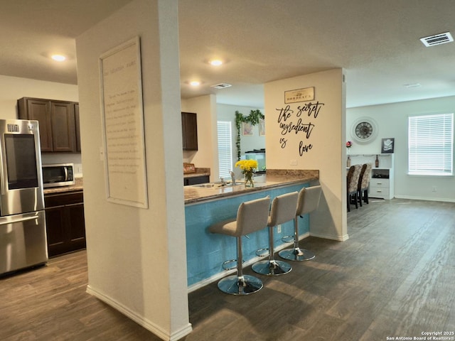 kitchen featuring visible vents, stainless steel appliances, dark brown cabinetry, a breakfast bar area, and dark wood-style flooring