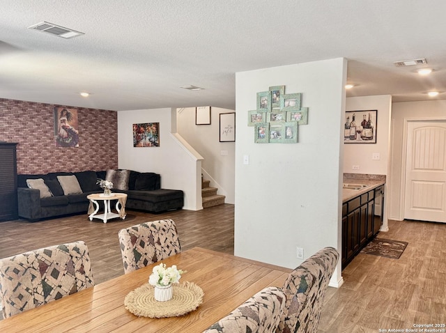 dining room with visible vents, light wood-style flooring, stairway, and a textured ceiling