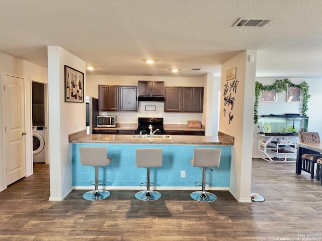 kitchen featuring visible vents, a peninsula, washer / dryer, dark brown cabinetry, and appliances with stainless steel finishes