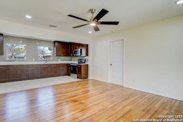 kitchen with light wood finished floors, stainless steel microwave, light countertops, decorative backsplash, and range with electric stovetop