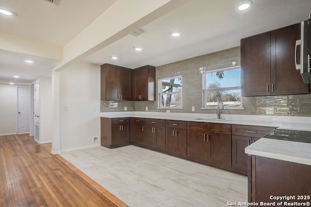 kitchen with a sink, backsplash, light wood-style floors, dark brown cabinetry, and light countertops