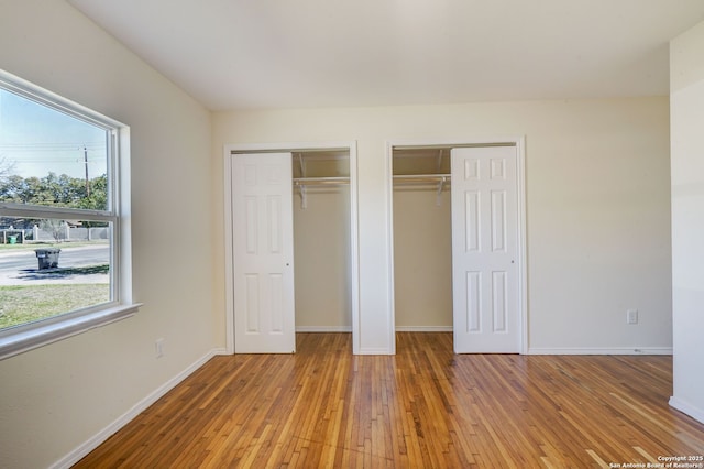 unfurnished bedroom featuring multiple windows, baseboards, light wood-style floors, and multiple closets