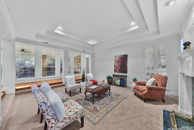 living area featuring crown molding, baseboards, carpet, a fireplace with flush hearth, and a tray ceiling