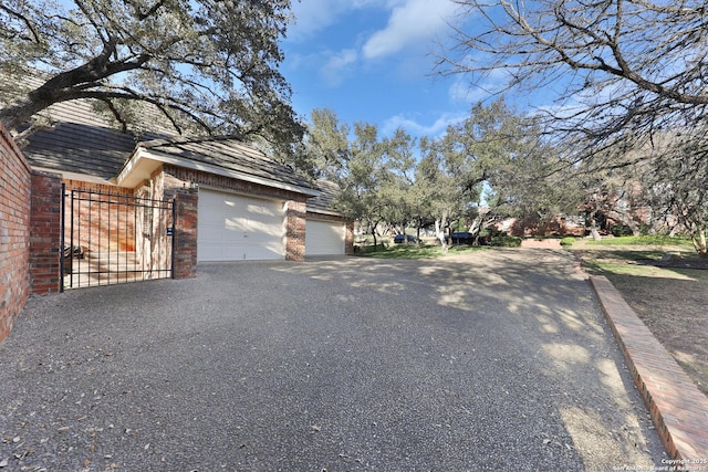 view of home's exterior with aphalt driveway, brick siding, an attached garage, and a gate