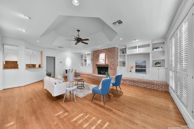 living room with visible vents, a brick fireplace, wood finished floors, a raised ceiling, and a ceiling fan