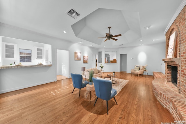 living area featuring light wood finished floors, visible vents, a fireplace, a raised ceiling, and a ceiling fan