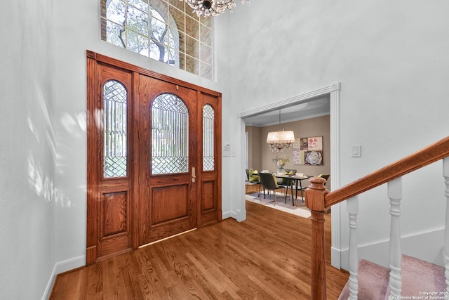 foyer entrance with wood finished floors, baseboards, stairs, a towering ceiling, and a chandelier