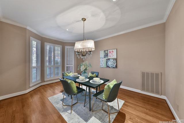 dining room with wood finished floors, baseboards, visible vents, ornamental molding, and a chandelier