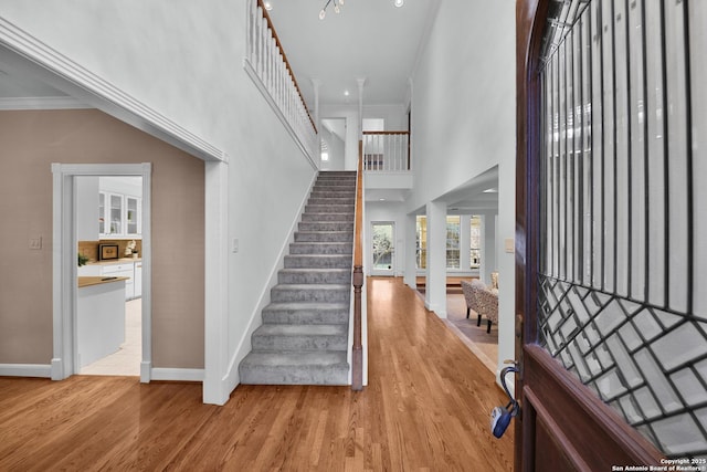 entryway featuring light wood-type flooring, a high ceiling, crown molding, and stairway