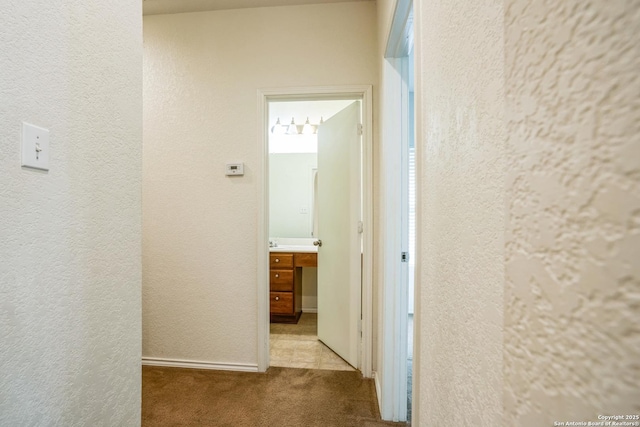 hallway featuring baseboards, carpet, and a textured wall