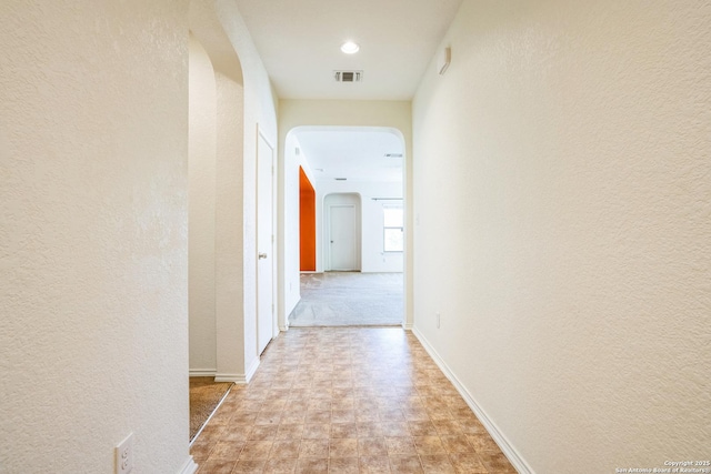 hall with visible vents, arched walkways, a textured wall, and baseboards