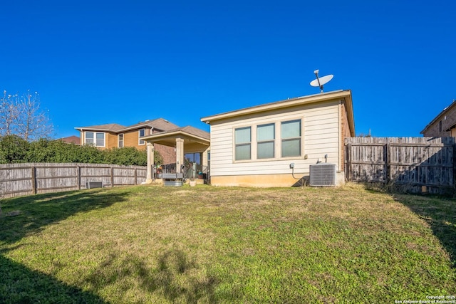 rear view of property with a fenced backyard, a lawn, and central AC