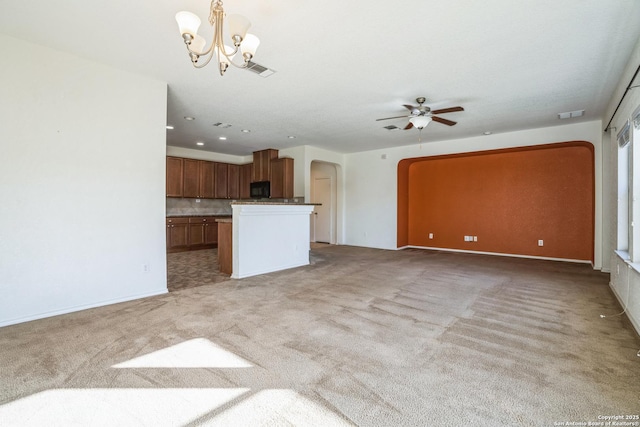 unfurnished living room with visible vents, ceiling fan with notable chandelier, arched walkways, and light carpet