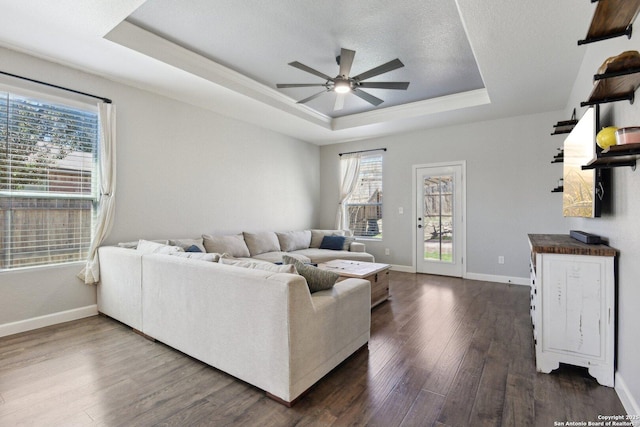 living area featuring dark wood-style floors, baseboards, a tray ceiling, ceiling fan, and a textured ceiling