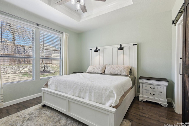 bedroom with crown molding, baseboards, dark wood-type flooring, a raised ceiling, and a ceiling fan