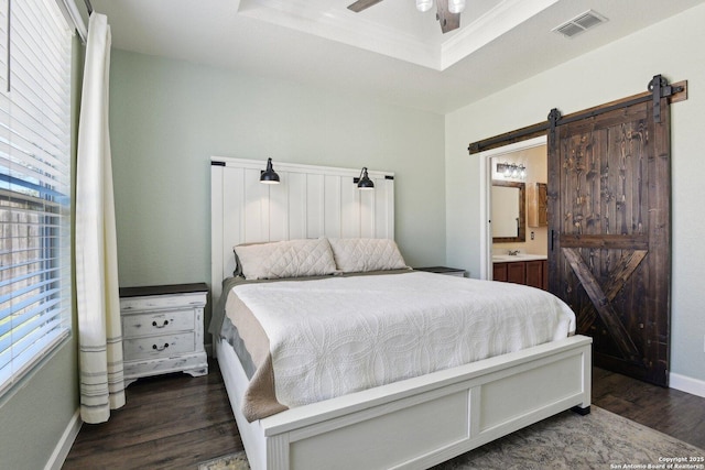 bedroom featuring visible vents, baseboards, a barn door, wood finished floors, and a raised ceiling