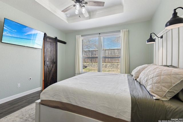 bedroom with wood finished floors, a barn door, baseboards, crown molding, and a raised ceiling