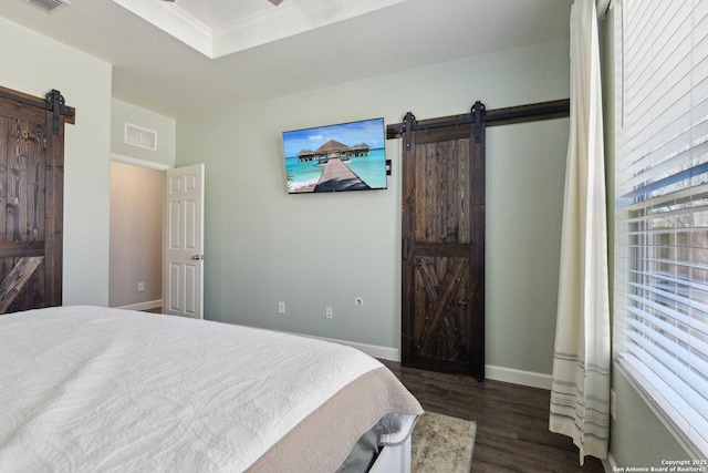 bedroom featuring visible vents, dark wood-type flooring, a tray ceiling, a barn door, and baseboards