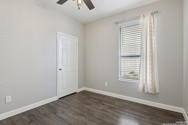 empty room featuring a ceiling fan, a healthy amount of sunlight, dark wood finished floors, and baseboards