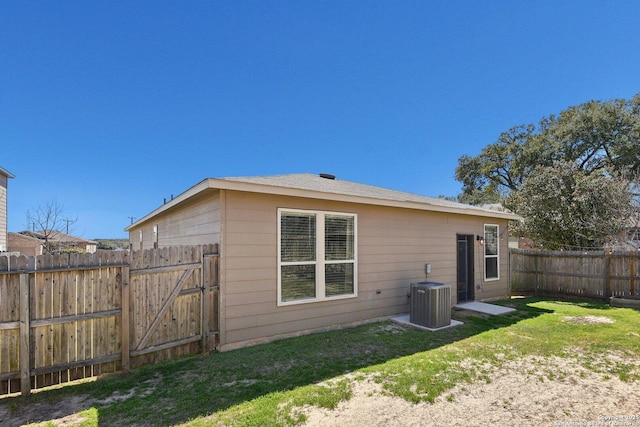 rear view of house with central air condition unit, a lawn, a fenced backyard, and a gate