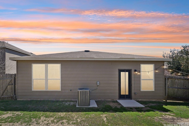 back of property at dusk with central air condition unit, a yard, and fence