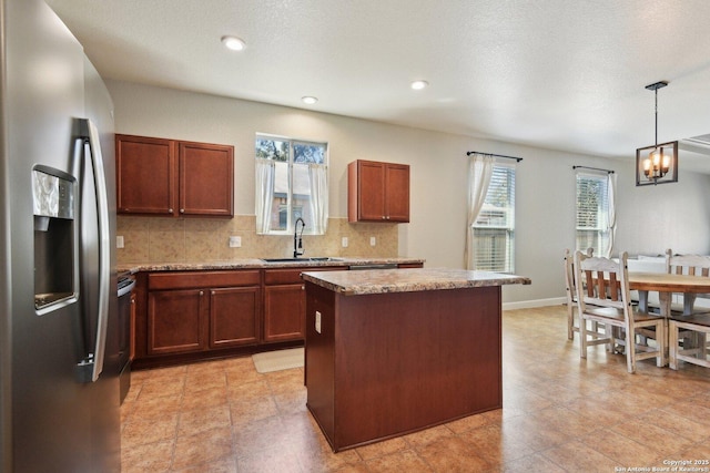 kitchen with stainless steel refrigerator with ice dispenser, a sink, backsplash, a center island, and hanging light fixtures