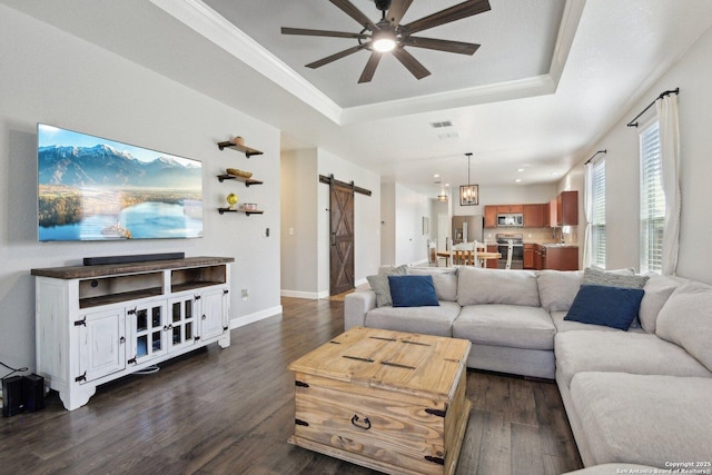 living area featuring a raised ceiling, dark wood-style floors, a barn door, baseboards, and ceiling fan