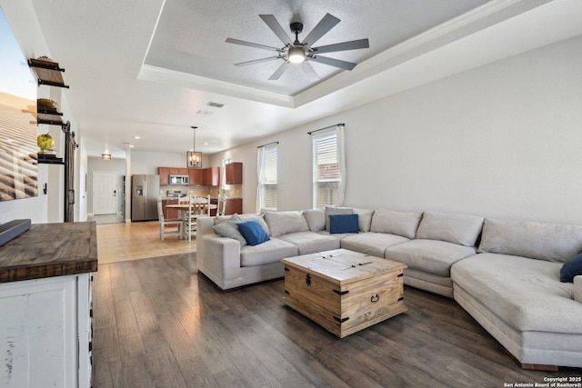 living area with visible vents, dark wood-type flooring, a textured ceiling, a raised ceiling, and ceiling fan