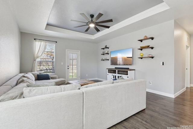 living area with baseboards, dark wood-style flooring, ceiling fan, a textured ceiling, and a raised ceiling