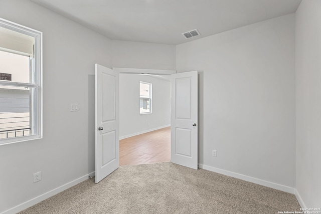 empty room featuring visible vents, baseboards, and light colored carpet