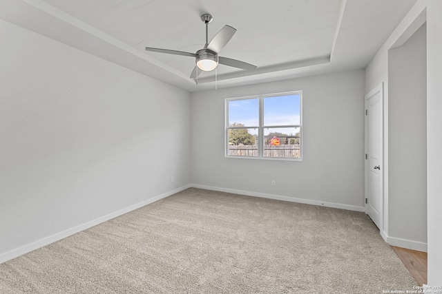 spare room featuring a tray ceiling, a ceiling fan, baseboards, and light carpet