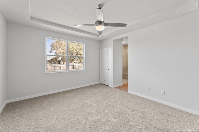 unfurnished bedroom featuring visible vents, a raised ceiling, ensuite bathroom, carpet floors, and baseboards