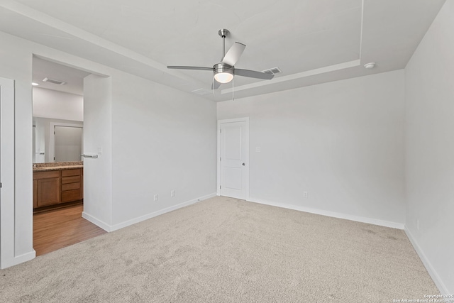 unfurnished bedroom featuring visible vents, light colored carpet, a raised ceiling, and baseboards