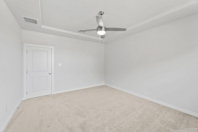 carpeted spare room featuring a raised ceiling, baseboards, visible vents, and ceiling fan