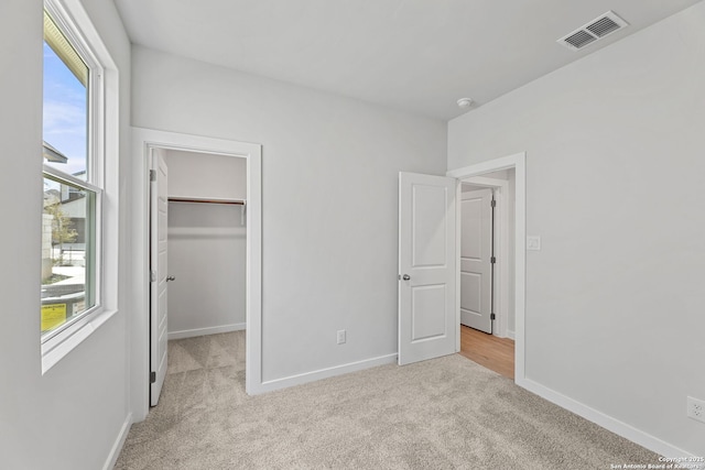 unfurnished bedroom with a spacious closet, baseboards, visible vents, and light carpet