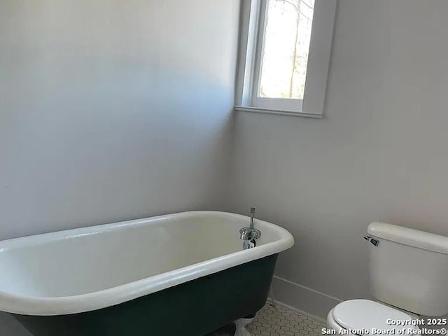 bathroom with a soaking tub, toilet, and baseboards