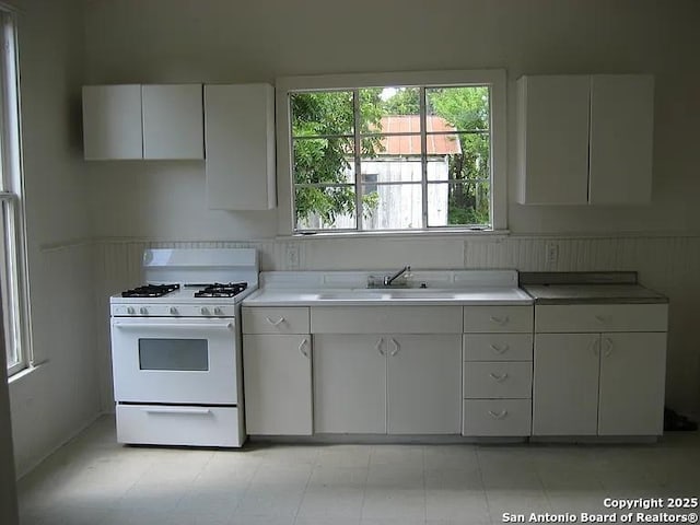 kitchen with a sink, white cabinetry, white gas stove, and light countertops